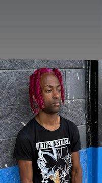 a man with pink dreadlocks standing next to a brick wall